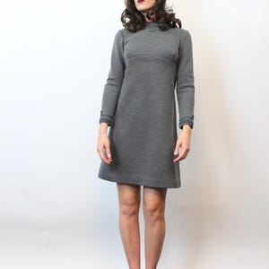 May include: A gray, long-sleeved dress with a round neckline and decorative cuffs. The dress is paired with a brown fur hat and gold-colored shoes with fringe.