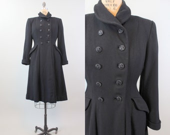 May include: A black double-breasted wool coat with a fitted waist and a flared skirt. The coat has a high collar and is fastened with black buttons.