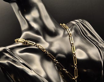 Puede incluir: Un collar de cadena dorada con un gran colgante de perla barroca blanca. El collar está en un maniquí negro.