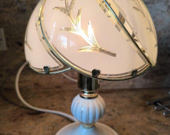 May include: A white table lamp with a gold-trimmed, floral-patterned glass shade. The lamp has a white base with a gold accent.