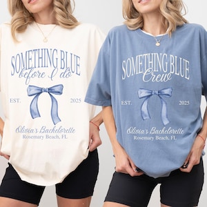 May include: Two t-shirts, one cream and one blue, with the text "SOMETHING BLUE" and a watercolor bow design. The cream shirt says "before I do" and the blue shirt says "Crew". Both shirts include "EST. 2025" and "Olivia's Bachelorette, Rosemary Beach, FL."