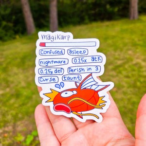 Może przedstawiać: Naklejka przedstawiająca czerwoną i żółtą rybę z kreskówki z napisem "magiKarp". Naklejka zawiera różne efekty statusu i statystyki, takie jak "Confused", "asleep" i "0.25x atk". Tło jest rozmyte zielone.
