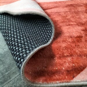 May include: A rolled-up rug with a watercolor design in shades of orange, pink, and white. The underside features a black and gray checkered pattern. The rug's edge is finished with a gray border.
