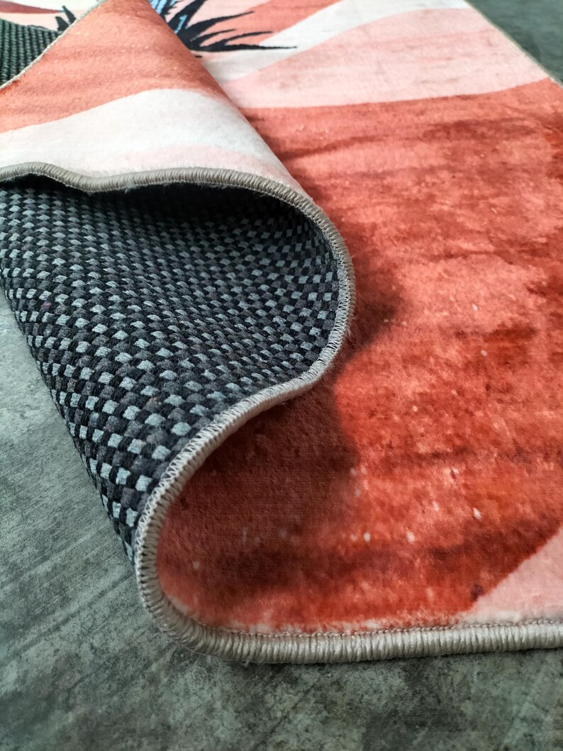 May include: A rolled-up rug with a watercolor design in shades of orange, pink, and white. The underside features a black and gray checkered pattern. The rug's edge is finished with a gray border.