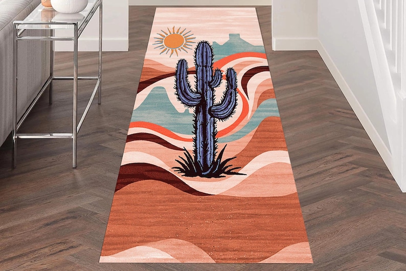 May include: A rectangular runner rug with a desert landscape design. The rug features a large blue cactus in the center, a sun, and layered earth-tone colors. The rug is designed to be placed in a hallway or entryway.