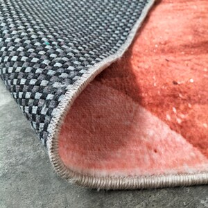 May include: Close-up of a rug with a gray and black checkered underside and a peach-colored top. The edge of the rug is visible, showing the stitching and the contrast between the two sides.