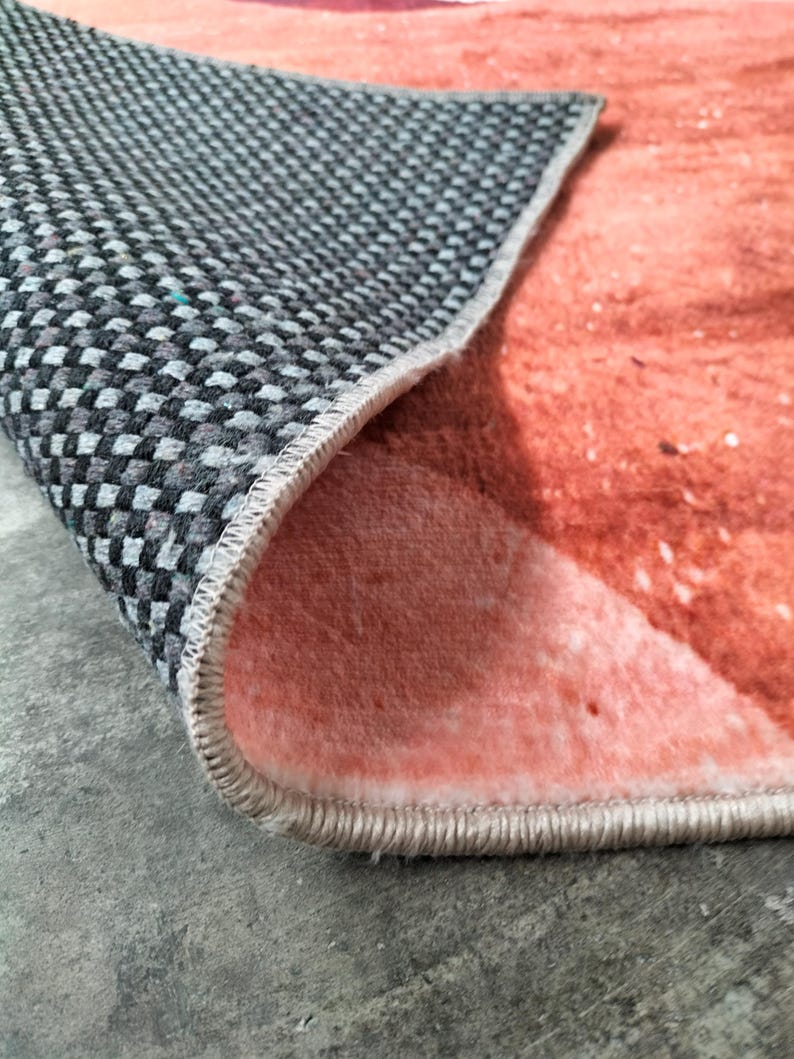 May include: Close-up of a rug with a gray and black checkered underside and a peach-colored top. The edge of the rug is visible, showing the stitching and the contrast between the two sides.
