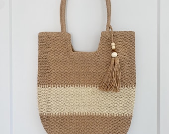 May include: A tan and white woven tote bag with a tassel and wooden beads. The bag has a wide, open top and a single strap.