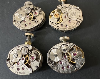 May include: Four antique watch movements with intricate gears and a silver finish. The movements are labeled "SEMCO" and "SWISS MADE".