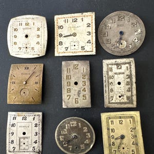 May include: A collection of nine vintage watch faces in various shapes, including square and round. The faces are off-white with black numerals and hands, showing signs of age and wear. Some have brand names like "BENRUS" and "CHALET".