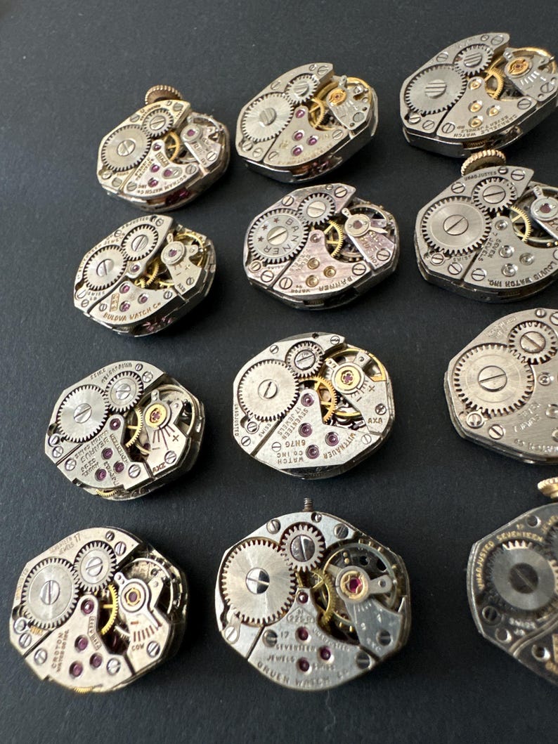 May include: A collection of vintage watch movements, showcasing intricate gears, jewels, and metallic components. The open-faced mechanisms display a variety of shapes and sizes, with visible text and details. The watch parts are arranged on a dark surface.