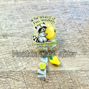 May include: A badge reel with a glittery yellow lemon charm and a raccoon holding a lemon with the text "In the interest of full transparency it was not easy peasy lemon squeezy".