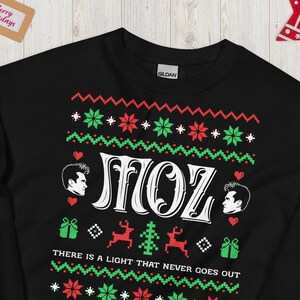 May include: Black Christmas jumper with a red and green pattern. It features the text "MOZ" and the phrase "There is a light that never goes out".
