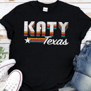 May include: Black t-shirt with a vintage-style graphic that says "KATY Texas" in white text with a red star and colorful stripes.