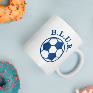May include: White ceramic mug with a blue soccer ball graphic and the text "B.L.U.R." printed on the side.
