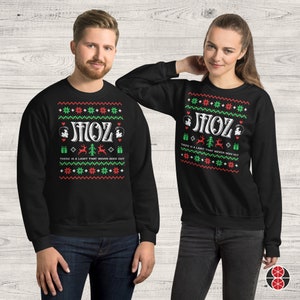 May include: Black Christmas jumper with a white snowflake pattern and the text "There is a light that never goes out" and "MOZ" in a retro font. The jumper features a small graphic of a person's face.