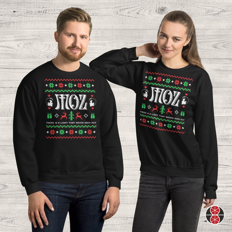 May include: Black Christmas jumper with a white snowflake pattern and the text "There is a light that never goes out" and "MOZ" in a retro font. The jumper features a small graphic of a person's face.