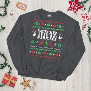 May include: A dark grey sweatshirt with a Christmas-themed design featuring two cartoon figures, the text "SMOZ", and the phrase "THERE IS A LIGHT THAT NEVER GOES OUT".