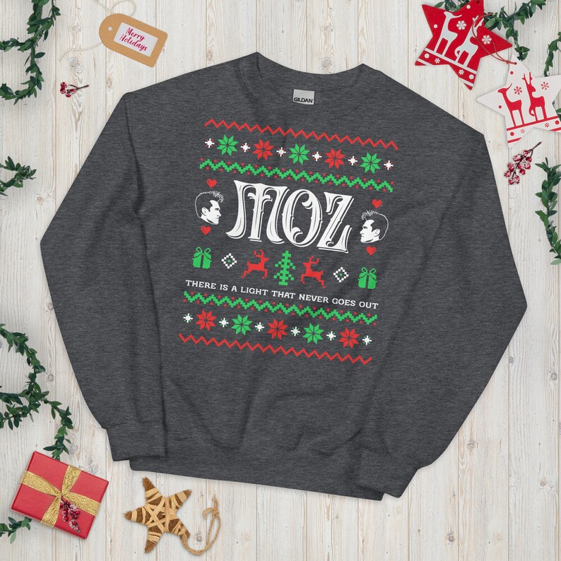 May include: A dark grey sweatshirt with a Christmas-themed design featuring two cartoon figures, the text "SMOZ", and the phrase "THERE IS A LIGHT THAT NEVER GOES OUT".