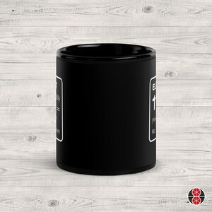 Puede incluir: Una taza de cer&aacute;mica negra con texto blanco y borde blanco. El texto incluye la palabra "EL" y el n&uacute;mero "119". La taza es cil&iacute;ndrica y est&aacute; sobre una superficie de madera clara.