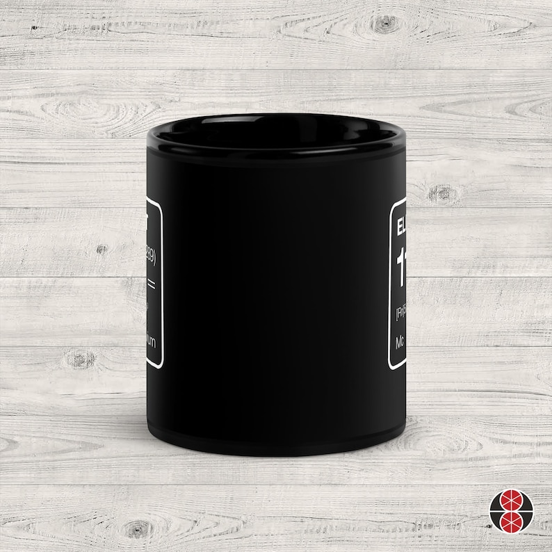 Puede incluir: Una taza de cer&aacute;mica negra con texto blanco y borde blanco. El texto incluye la palabra "EL" y el n&uacute;mero "119". La taza es cil&iacute;ndrica y est&aacute; sobre una superficie de madera clara.