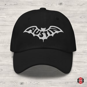 May include: Black baseball cap with a white embroidered bat design featuring the word "Austin".