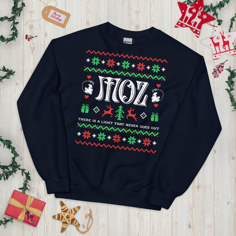May include: A navy blue Christmas jumper with a white, green and red design. It features the text "SMOZ" and the phrase "THERE IS A LIGHT THAT NEVER GOES OUT".