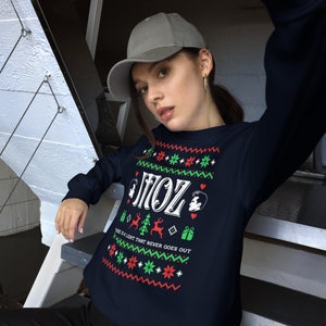 May include: A navy blue Christmas jumper with a white design featuring the text "Moz" and a reindeer. The jumper has a red and green pattern with snowflakes and hearts. The text "There is a light that never goes out" is printed below the reindeer.