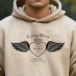 May include: A beige hoodie with a black print that says "In Loving Memory" with a heart and wings. The heart has a space to add a photo and the text "Add Photo". Below the heart is the text "NAME HERE 01.05.1954 - 12.08.2023".