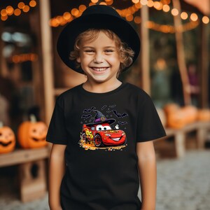Puede incluir: Una camiseta negra con un gr&aacute;fico de un coche de carreras rojo con el n&uacute;mero 95, que lleva un sombrero de bruja negro con borde morado, rodeado de murci&eacute;lagos negros y peque&ntilde;os trozos de caramelo de ma&iacute;z en la parte frontal.