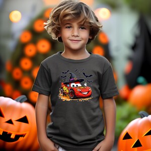 Puede incluir: Una camiseta gris oscuro de manga corta con un gr&aacute;fico de un coche de carreras rojo con el n&uacute;mero 95, que lleva un sombrero de bruja negro. El dise&ntilde;o incluye peque&ntilde;os murci&eacute;lagos negros, un fantasma blanco y caramelos naranjas en la tela.