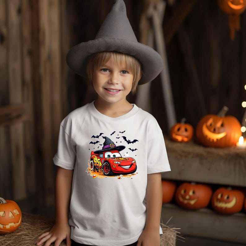 Puede incluir: Una camiseta blanca de manga corta con un gr&aacute;fico de un coche de carreras rojo con el n&uacute;mero 95, que lleva un sombrero de bruja negro. El dise&ntilde;o incluye siluetas negras de murci&eacute;lagos volando y peque&ntilde;os caramelos de color naranja.