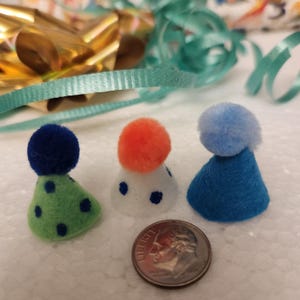 Peut inclure: Trois petits chapeaux de fête avec des pompons sur le dessus. Les chapeaux sont verts à pois bleus, blancs à pois bleus et bleus.