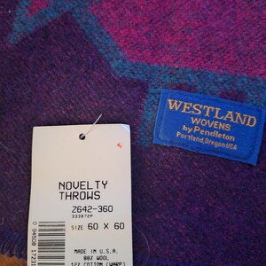 May include: A purple and magenta novelty throw with a geometric teal design. The throw measures 152 x 152 cm and is made of 88% wool and 12% cotton. The tag reads "Westland Wovens by Pendleton, Portland, Oregon USA."