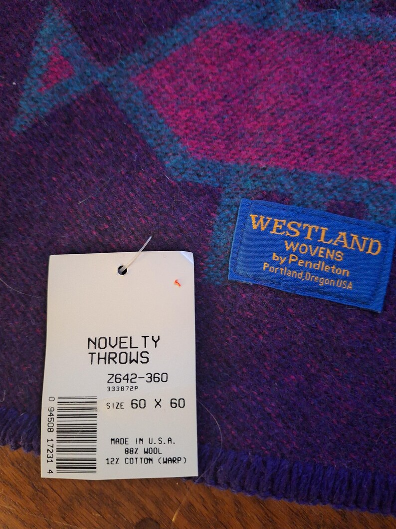 May include: A purple and magenta novelty throw with a geometric teal design. The throw measures 152 x 152 cm and is made of 88% wool and 12% cotton. The tag reads "Westland Wovens by Pendleton, Portland, Oregon USA."