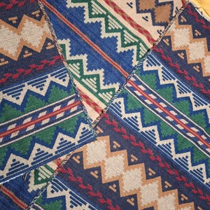 Peut inclure: Gros plan sur un textile patchwork avec un motif g&eacute;om&eacute;trique. Le motif pr&eacute;sente des zigzags, des triangles et des losanges dans des tons de bleu, vert, beige et rouge. Le textile est probablement en tissu tiss&eacute;.