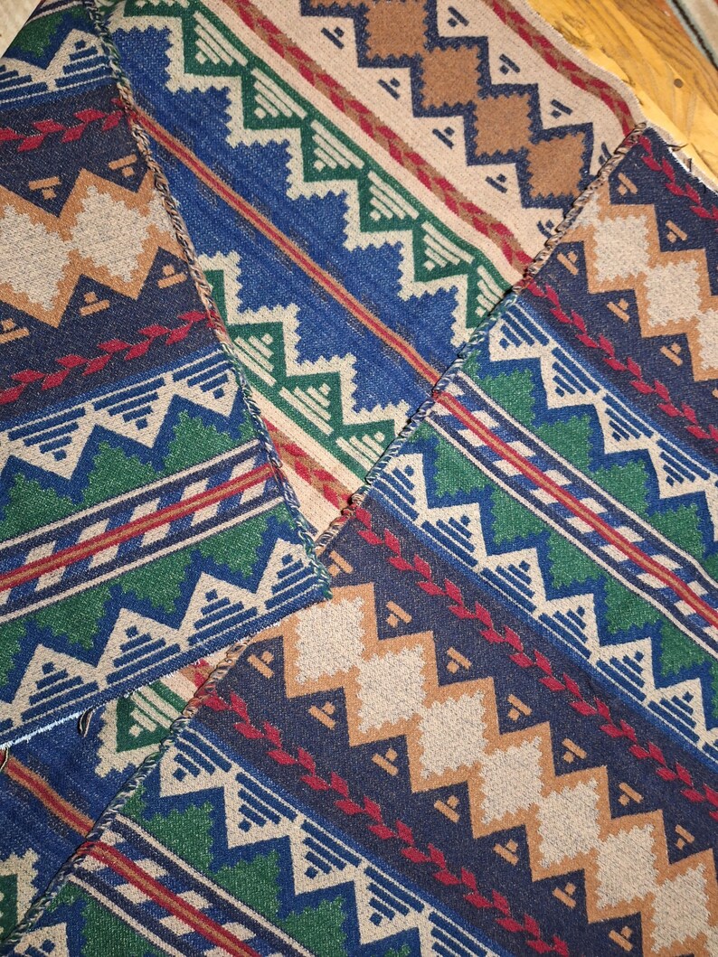 Peut inclure: Gros plan sur un textile patchwork avec un motif g&eacute;om&eacute;trique. Le motif pr&eacute;sente des zigzags, des triangles et des losanges dans des tons de bleu, vert, beige et rouge. Le textile est probablement en tissu tiss&eacute;.