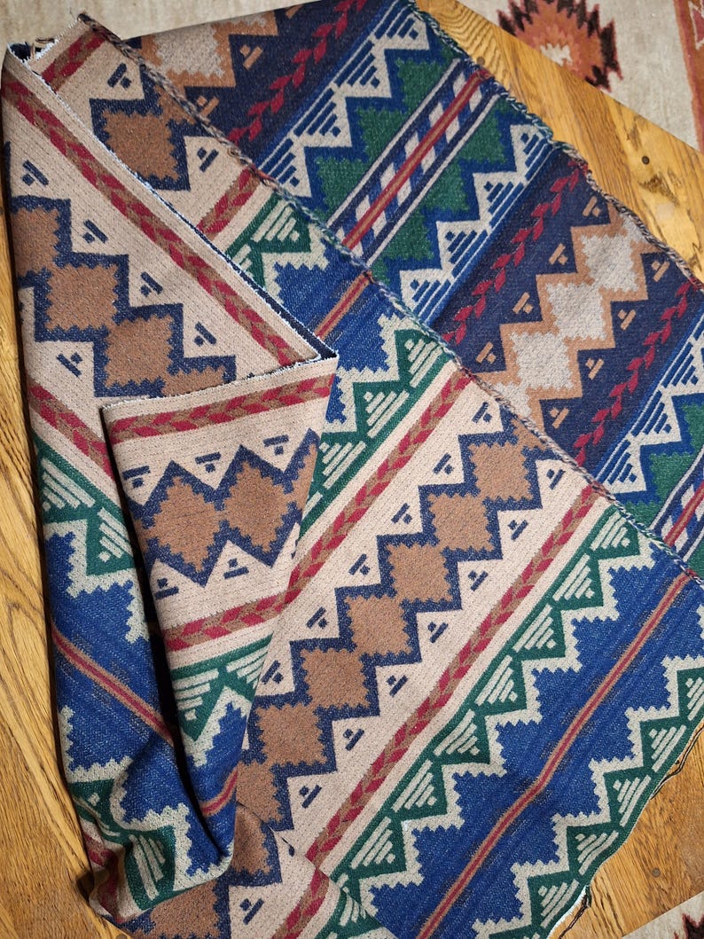 Peut inclure: Textile pli&eacute; avec un motif g&eacute;om&eacute;trique dans les tons de marron, bleu, vert et rouge. Le motif pr&eacute;sente des zigzags et des losanges. Le tissu semble &ecirc;tre une mati&egrave;re tiss&eacute;e, peut-&ecirc;tre une couverture ou un jet&eacute;.