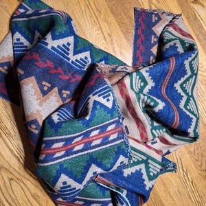 Peut inclure: &Eacute;charpe pli&eacute;e avec un motif g&eacute;om&eacute;trique dans les tons de bleu, vert, rouge et beige. L'&eacute;charpe a une texture tiss&eacute;e et un bord &agrave; franges. Le motif pr&eacute;sente des formes et des lignes r&eacute;p&eacute;titives.