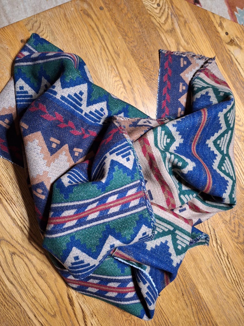 Peut inclure: &Eacute;charpe pli&eacute;e avec un motif g&eacute;om&eacute;trique dans les tons de bleu, vert, rouge et beige. L'&eacute;charpe a une texture tiss&eacute;e et un bord &agrave; franges. Le motif pr&eacute;sente des formes et des lignes r&eacute;p&eacute;titives.