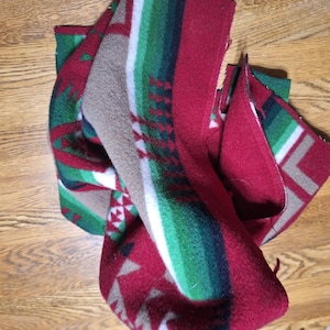 May include: A folded red, green, and white patterned blanket. The blanket has a striped design with green, white, and brown stripes. The blanket also has a geometric pattern in red, green, and brown.