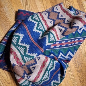 Peut inclure: Une couverture pli&eacute;e avec un motif du Sud-Ouest. La couverture pr&eacute;sente un fond bleu avec des formes g&eacute;om&eacute;triques blanches, vertes, rouges et marron. La couverture est faite d'une mati&egrave;re douce et est pli&eacute;e sur une surface en bois.