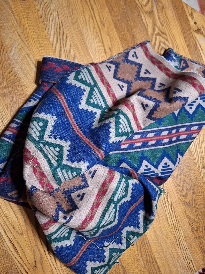 Peut inclure: Une couverture pli&eacute;e avec un motif du Sud-Ouest. La couverture pr&eacute;sente un fond bleu avec des formes g&eacute;om&eacute;triques blanches, vertes, rouges et marron. La couverture est faite d'une mati&egrave;re douce et est pli&eacute;e sur une surface en bois.