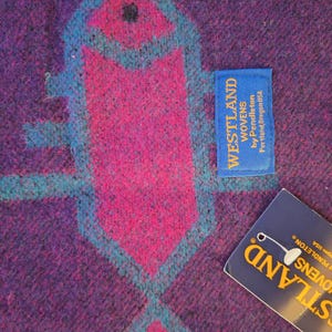 May include: Close-up of a woven textile with a geometric design in shades of purple, pink, and teal. The design features a central arrow-like shape. A blue tag reads "WESTLAND WOVENS by Pendleton Portland, Oregon USA."