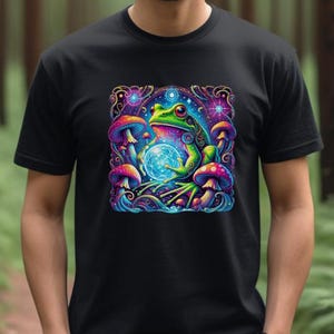 May include: Black t-shirt with a colourful, psychedelic design. The graphic shows a green frog holding a glowing orb, surrounded by vibrant mushrooms and celestial elements. The artwork is detailed and visually striking.