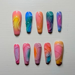 Peut inclure: Ensemble de dix faux ongles avec un design ombré coloré. Chaque ongle a un tourbillon de rose, bleu, jaune et orange.