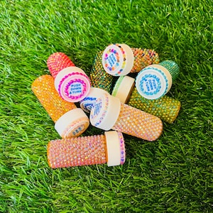 May include: A group of small, clear bottles with colorful rhinestones covering the entire surface. The bottles have white caps with the words "PUSH DOWN & TURN" printed on them.