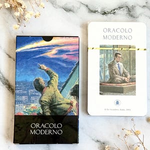 May include: A deck of oracle cards and a single card. The card box features a painting of a person pointing at a meteor shower over a city. The text "ORACLO MODERNO" is at the bottom. The single card has the same text.