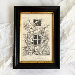 May include: Black framed artwork with a gold inner border. The artwork is a black and white etching of a window and door surrounded by foliage. The artist's signature and edition number are visible.