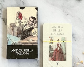 Könnte beinhalten: Zwei Kartenspiele im antiken Stil. Eine Schachtel zeigt einen Mann, der Pfeife raucht, die andere eine Frau in einem roten Kleid. Beide Schachteln tragen die Aufschrift "ANTICA SIBILLA ITALIANA". Die Decks sind mit einem goldenen Band gebunden.